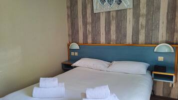 A neatly made bed with white linens and towels, a wooden headboard, and a wall-mounted sign with the word "LOVE".