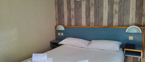 A neatly made bed with white linens and towels, a wooden headboard, and a wall-mounted sign with the word "LOVE".