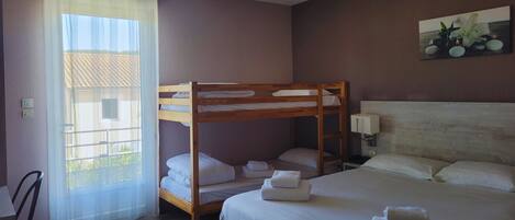 Un dormitorio con una cama individual, una litera, una ventana con cortinas traslúcidas, una lámpara de pared y un cuadro.