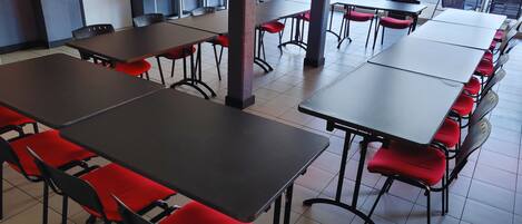 A cafeteria with multiple tables and chairs, a coffee machine, and a view of the outdoors.