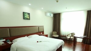 Quarto de hotel com uma cama grande, mesa de cabeceira com telefone, uma cadeira, uma pequena mesa e uma janela com cortinas.