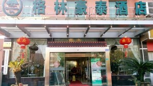 Entrada de hotel com placa em caracteres chineses, um lanterna vermelha e plantas em vasos.
