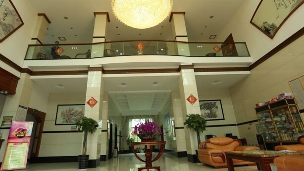 Um hall espaçoso com um lustre, tapete vermelho, assentos de couro e um guarda-corpo de vidro no nível superior.