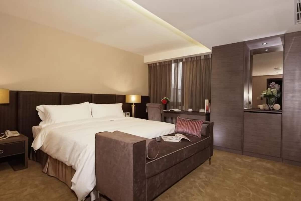 A hotel room with a large bed, bedside table, lamp, and a mirror.