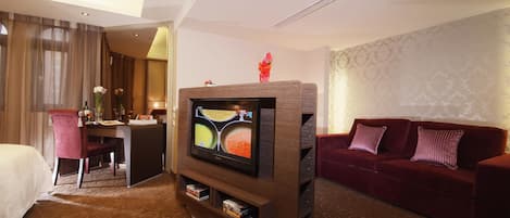A hotel room with a bed, a desk, a television, a red sofa, and a patterned carpet.