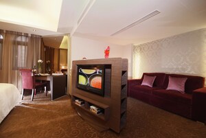 Een hotelkamer met een bed, een bureau, een televisie, een rode bank en een kamerbreed tapijt met dessin.