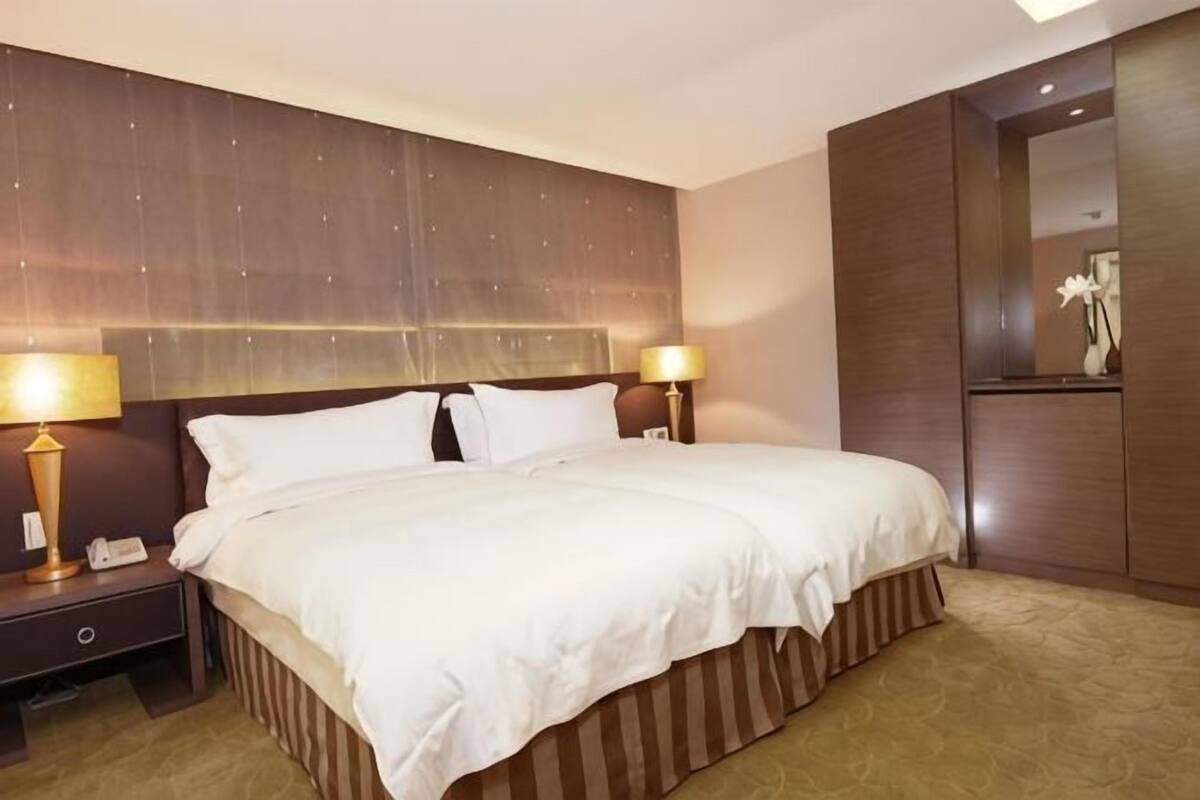 A hotel room with a large bed, two bedside tables with lamps, a nightstand, and a mirror.
