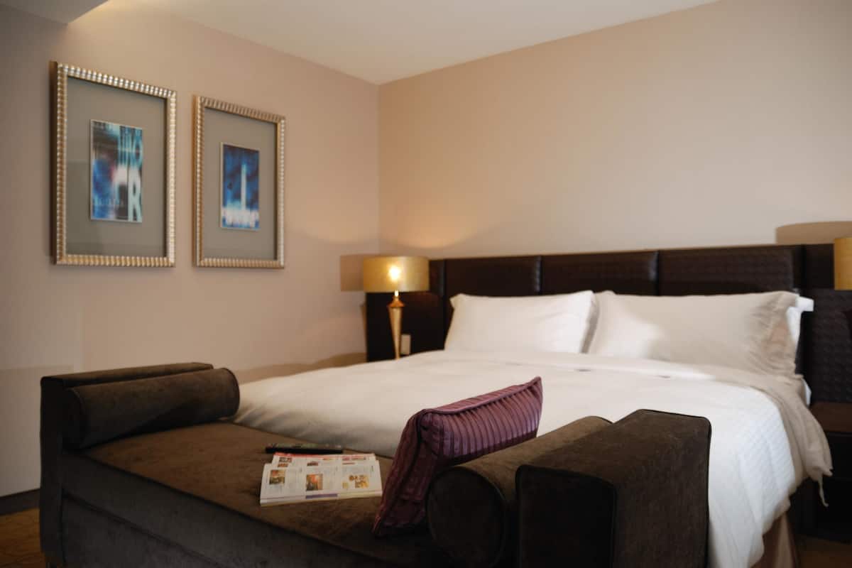 A hotel room with a bed, a sofa, two framed pictures on the wall, and a lamp.