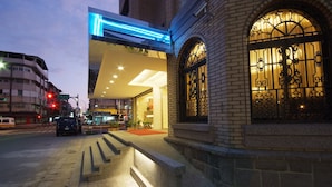 A hotel entrance with a modern facade, a red carpet, and a brick wall with decorative window grills. - The Metro Hotel (Taipei)