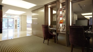 A modern hotel lobby with a glass partition, a reception desk, and a seating area with two chairs. - The Metro Hotel (Taipei)