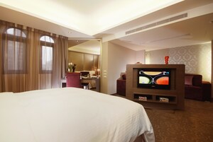Een hotelkamer met een groot bed, een televisie, een bureau met stoel en een bijzettafeltje met vaas.