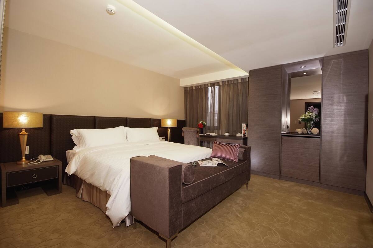 A hotel room with a large bed, bedside tables with lamps, a sofa, a mirror, and a dresser.
