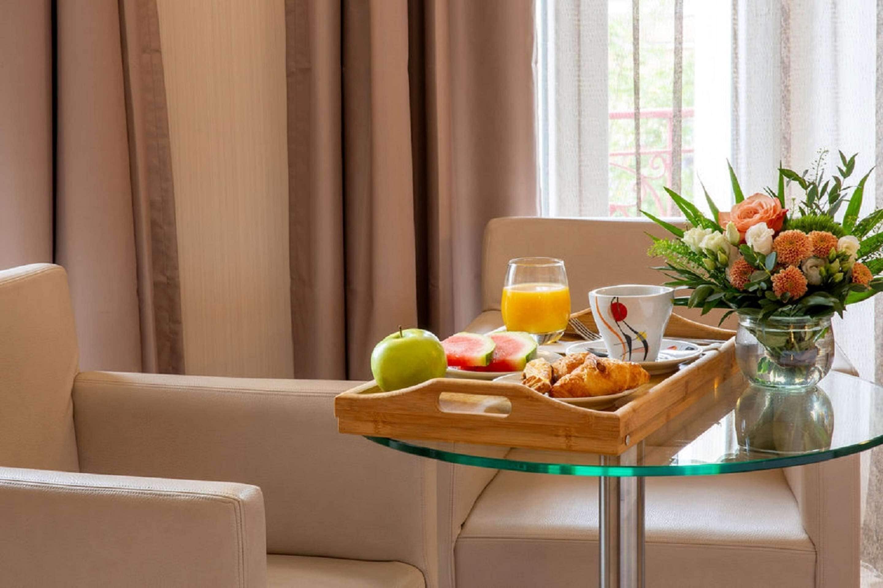Bandeja de desayuno con frutas, croissants y jugo sobre una mesa de vidrio en una habitación de hotel.