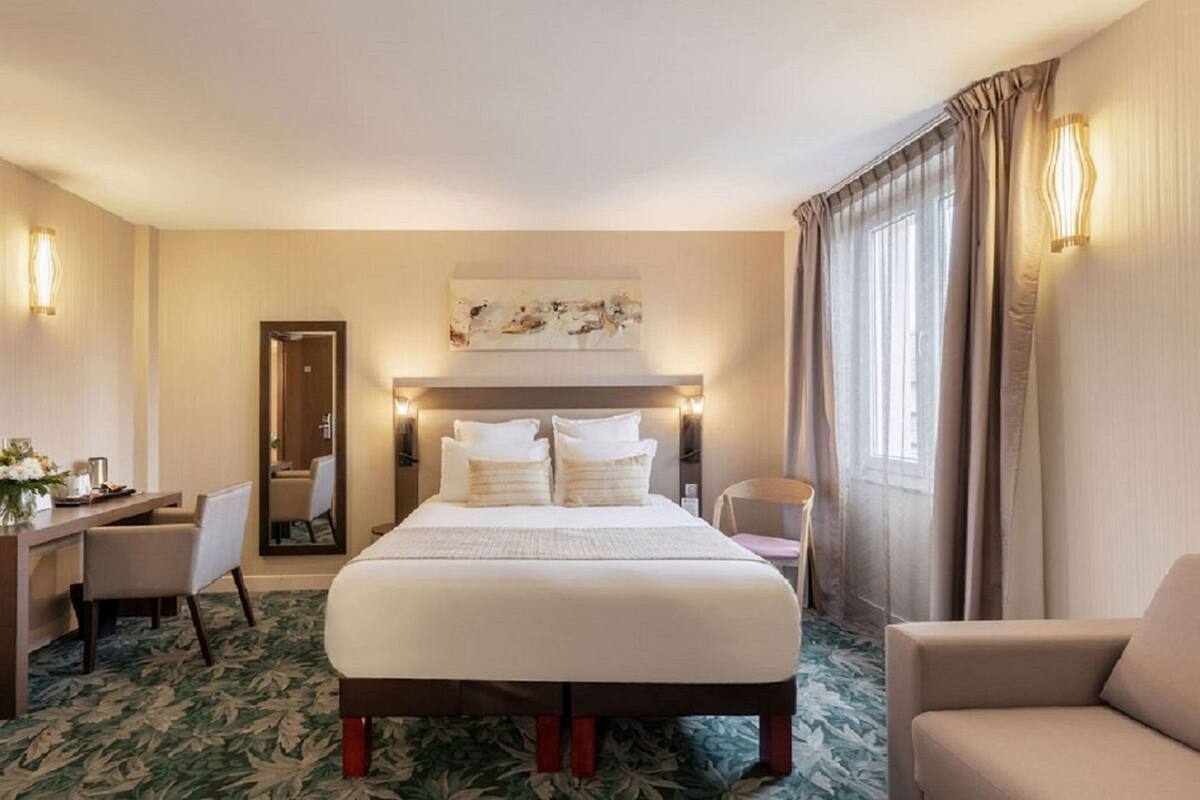 Ein Hotelzimmer mit einem großen Bett, einem Schreibtisch, einem Sessel, einem Spiegel und einem Fenster mit Vorhängen.