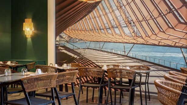 Un restaurant avec des chaises et des tables en osier, un mur végétal et une vue sur l’eau.
