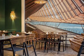 A restaurant with wicker chairs and tables, a green wall, and a view of the water. - Best Western Plus Hotel Belfort Centre Gare (Belfort)