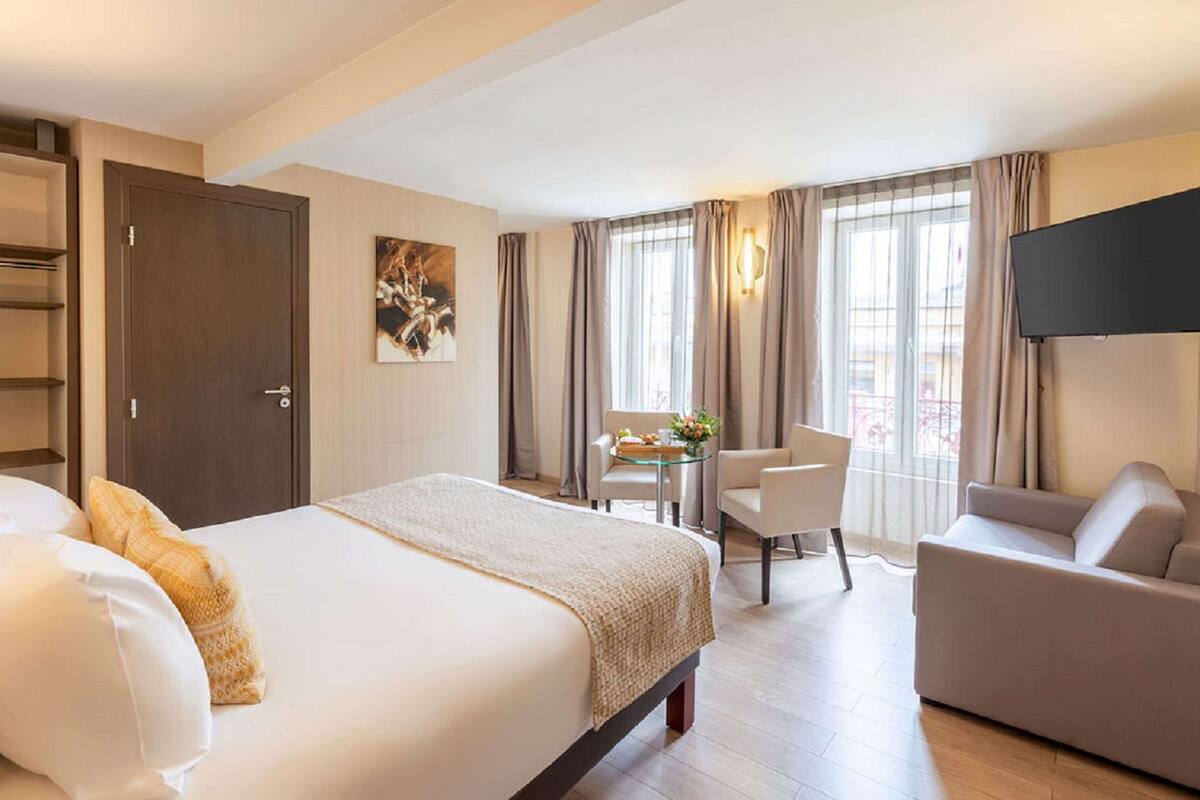 Ein Hotelzimmer mit Bett, Sofa, Fernseher, Schreibtisch mit Stuhl und einem Fenster mit Vorhängen.