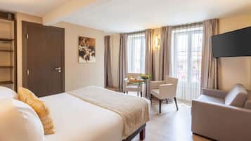 Une chambre d’hôtel comprenant un lit, un canapé, une télévision, un bureau avec une chaise et une fenêtre avec des rideaux.