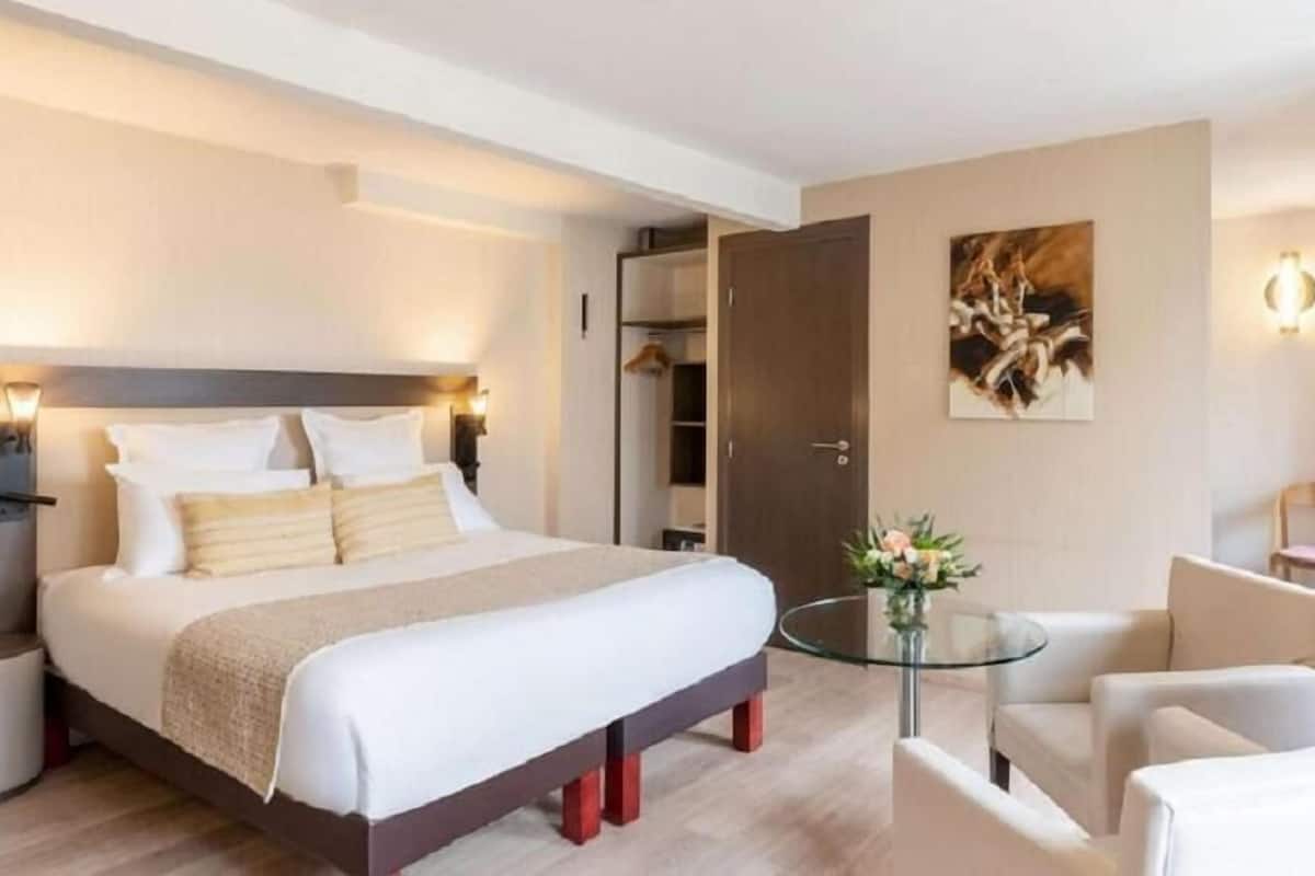 Ein modernes Hotelzimmer mit einem großen Bett, Nachttischen, einem Glastisch und einer Sitzecke mit Stühlen.