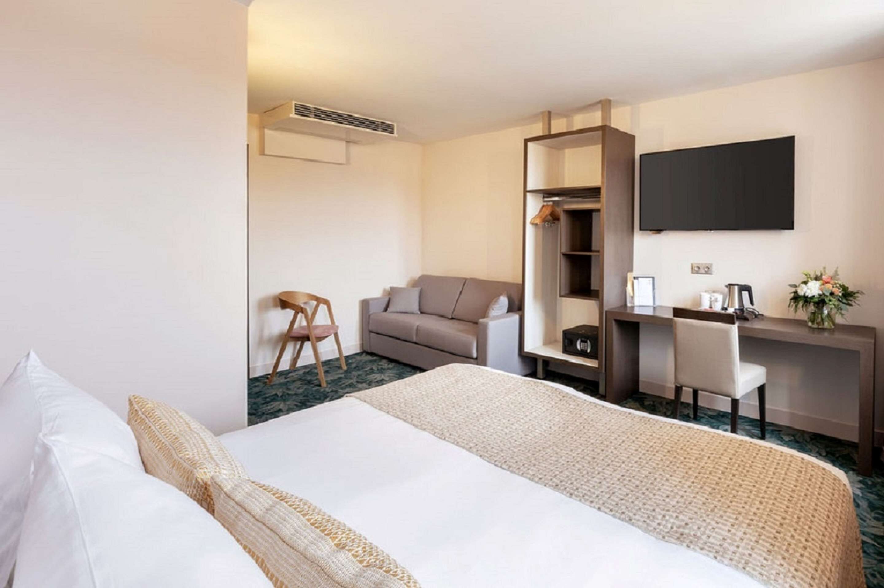 A hotel room with a bed, a desk, a chair, a sofa, a TV, and a wardrobe.