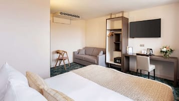 A hotel room with a bed, a desk, a chair, a sofa, a TV, and a wardrobe.