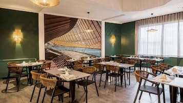 Un restaurante con una decoración moderna, que presenta un mural grande, mobiliario de mimbre e iluminación colgante.