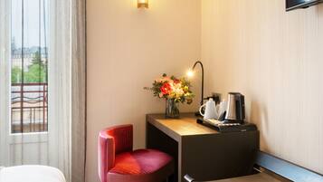 Une chambre d’hôtel avec un lit, un bureau agrémenté d’un vase de fleurs, une machine à café et un téléviseur fixé au mur.