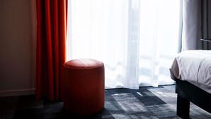 A hotel room with a bed, a red ottoman, and a large window with sheer curtains. - ibis Styles Bourbon Lancy (Bourbon-Lancy)