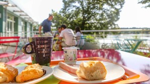 A table with food items and a beverage, set outdoors with a view of a body of water and trees in the background. - ibis Styles Bourbon Lancy (Bourbon-Lancy)