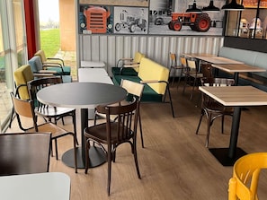 A restaurant with a mix of round and square tables, green and yellow cushioned seating, and a mural of vintage tractors.