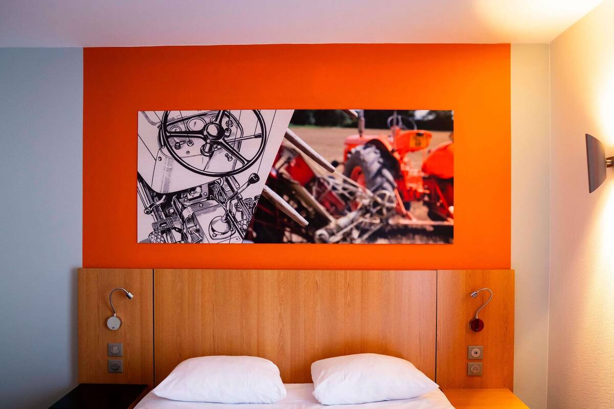 Una habitación de hotel con cama, dos mesitas de noche, cabecero y una obra de arte colgada en la pared.