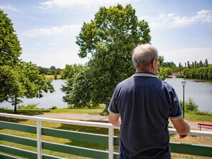 A man standing by a railing overlooking a lake with trees and a distant building. - ibis Styles Bourbon Lancy (Bourbon-Lancy)
