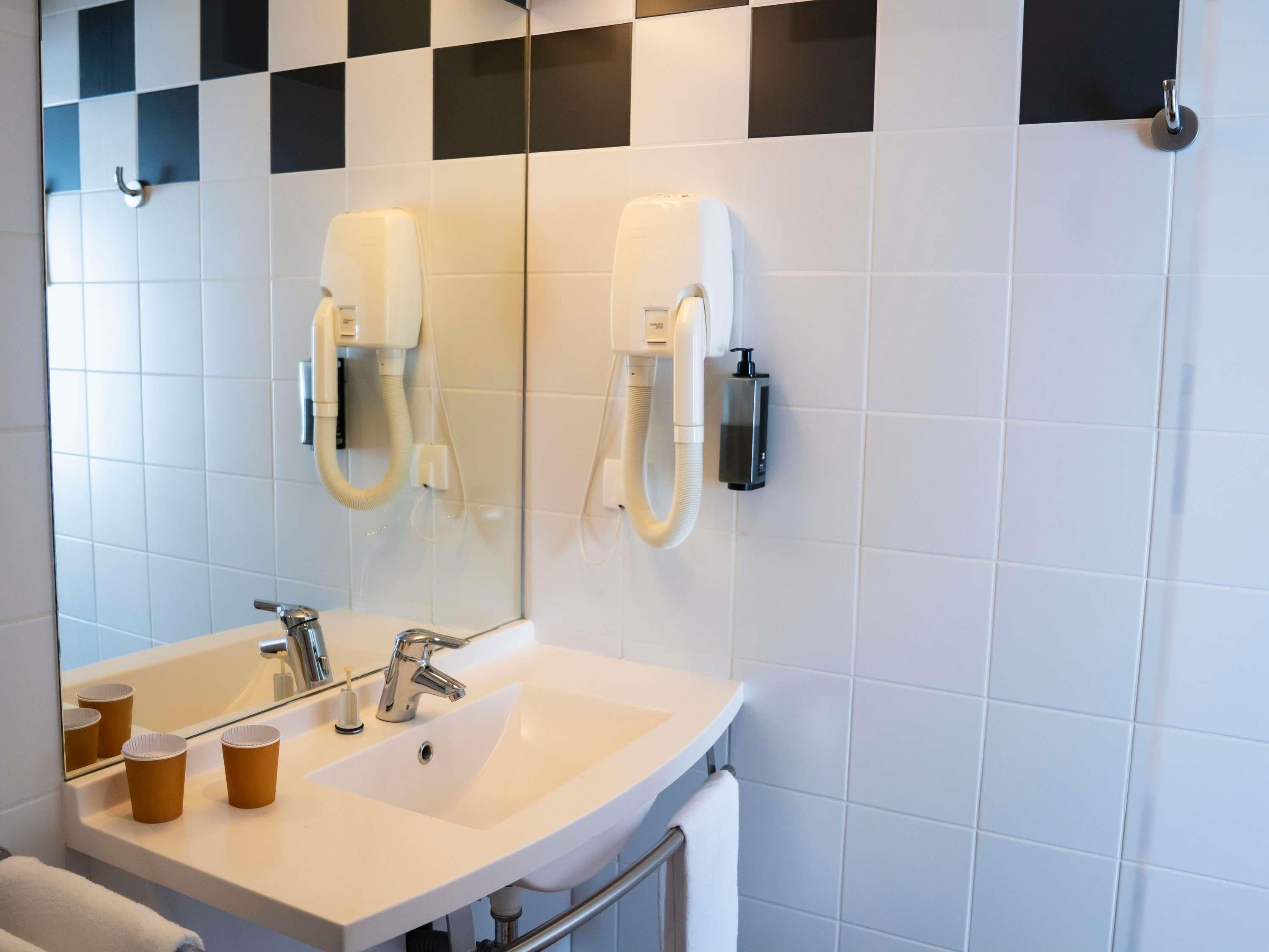 A bathroom with a sink, mirror, and two paper cups on the counter.