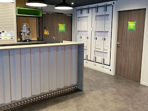 A reception area with a counter, a coffee machine, and a wall-mounted display. There are doors labeled with weight and volume limits.