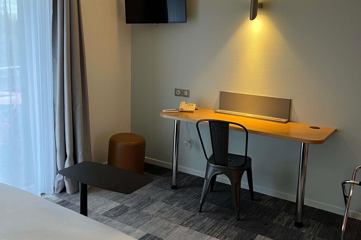 A modern hotel room with a desk, chair, and a flat-screen TV mounted on the wall.