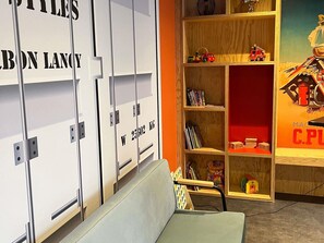 A room with a grey sofa, a wooden bookshelf with toys and books, and white lockers with weight labels. - ibis Styles Bourbon Lancy (Bourbon-Lancy)