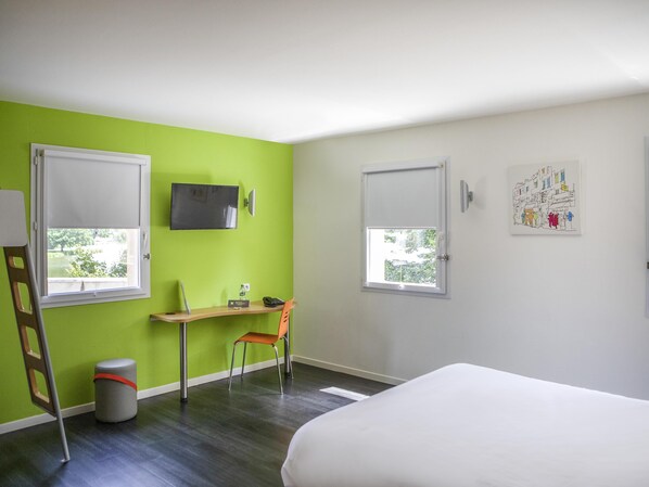 Una habitación con dos ventanas, un escritorio, una silla, una cama y un cubo de basura.