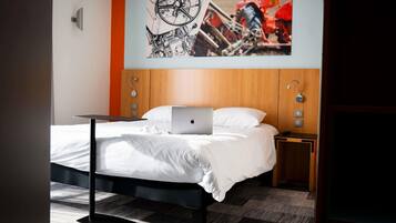 Une chambre d’hôtel comprenant un lit, un ordinateur portable, une table de chevet, une lampe fixée au mur et une œuvre d’art décorative.