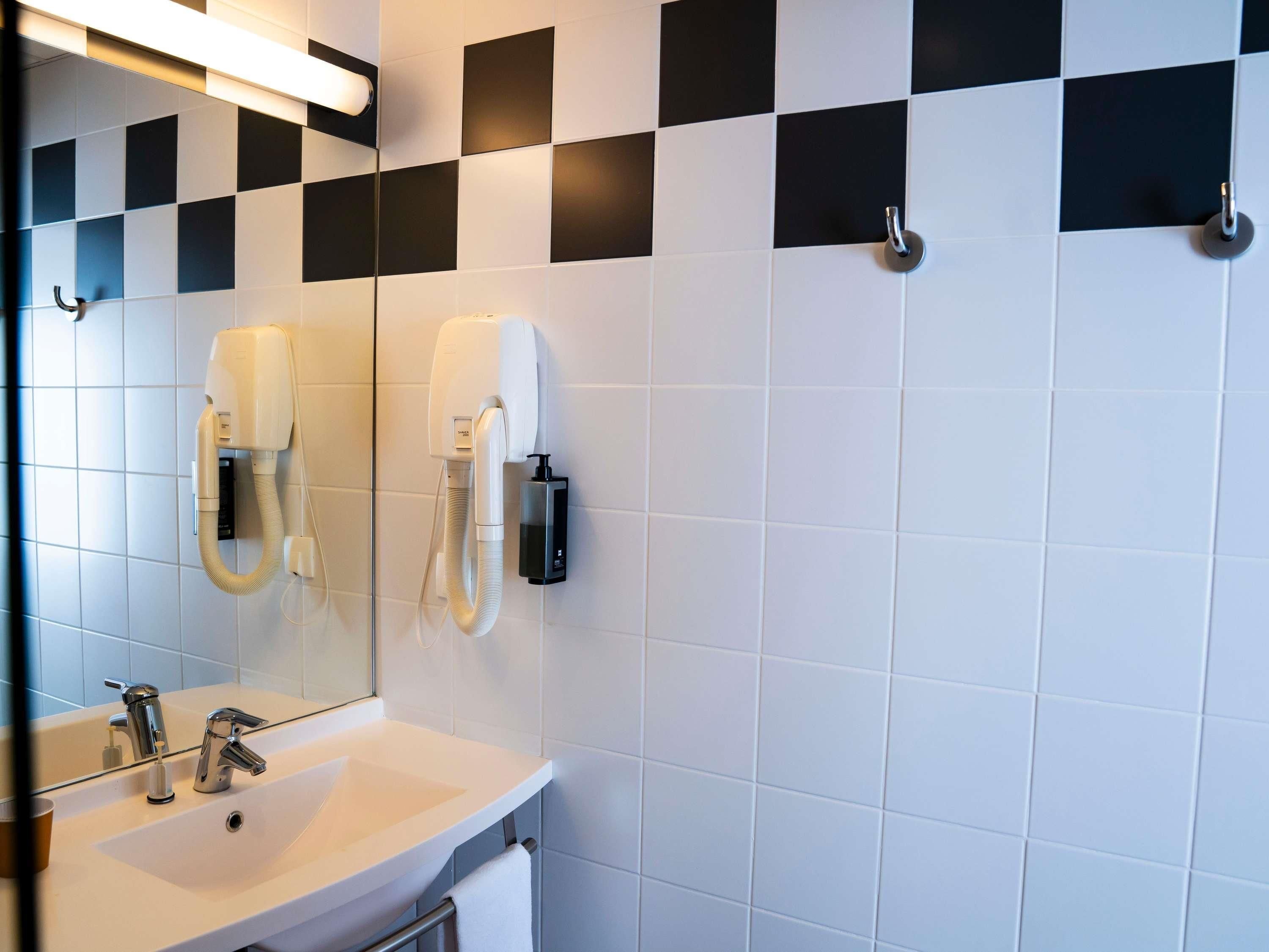 Un baño moderno con un lavabo blanco, dos espejos, un secador de pelo y un perchero para toallas.