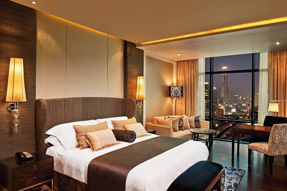 A hotel room with a large bed, a desk, and a view of the city skyline.