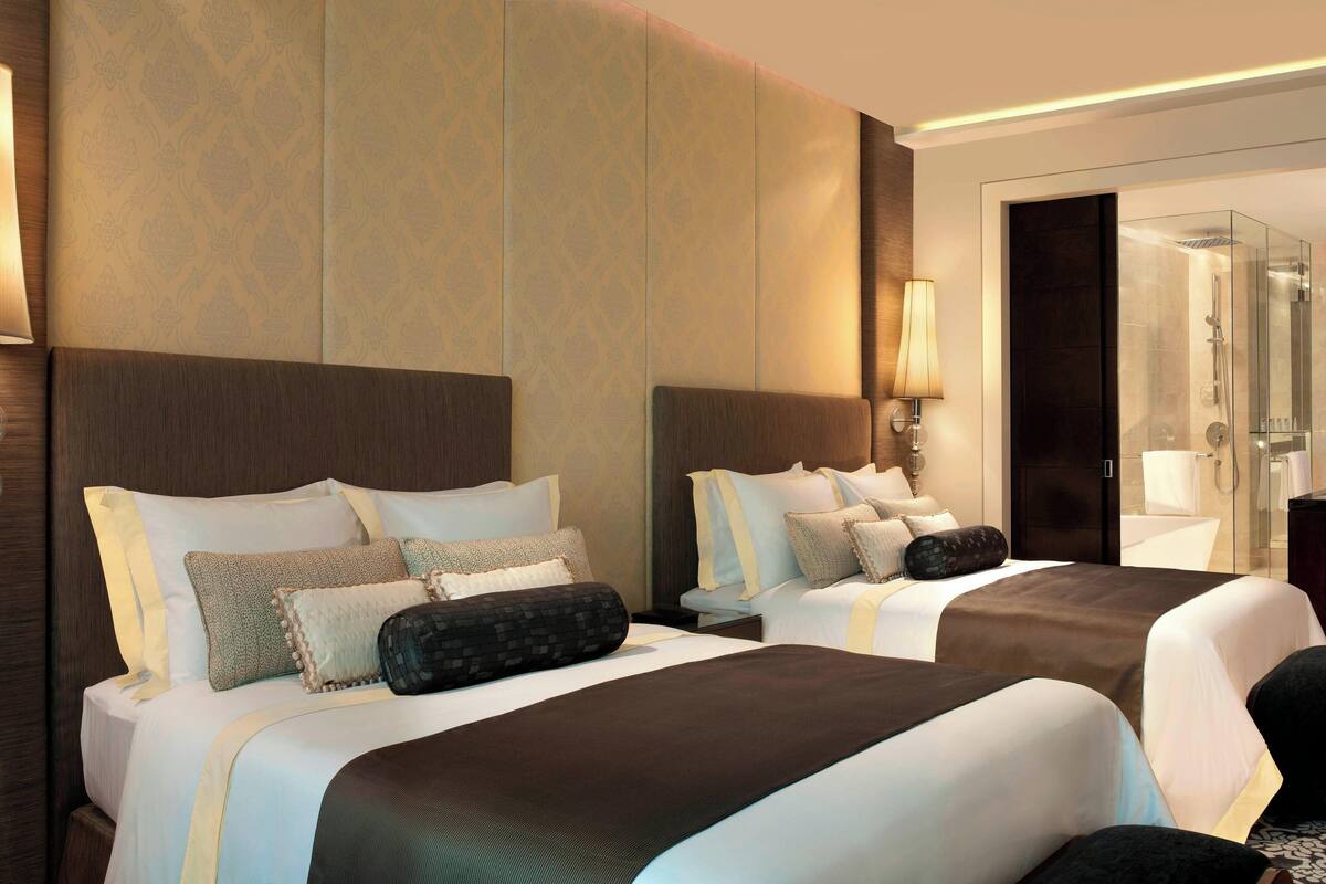 A hotel room with two beds, a large mirror, a glass shower enclosure, and a wardrobe.