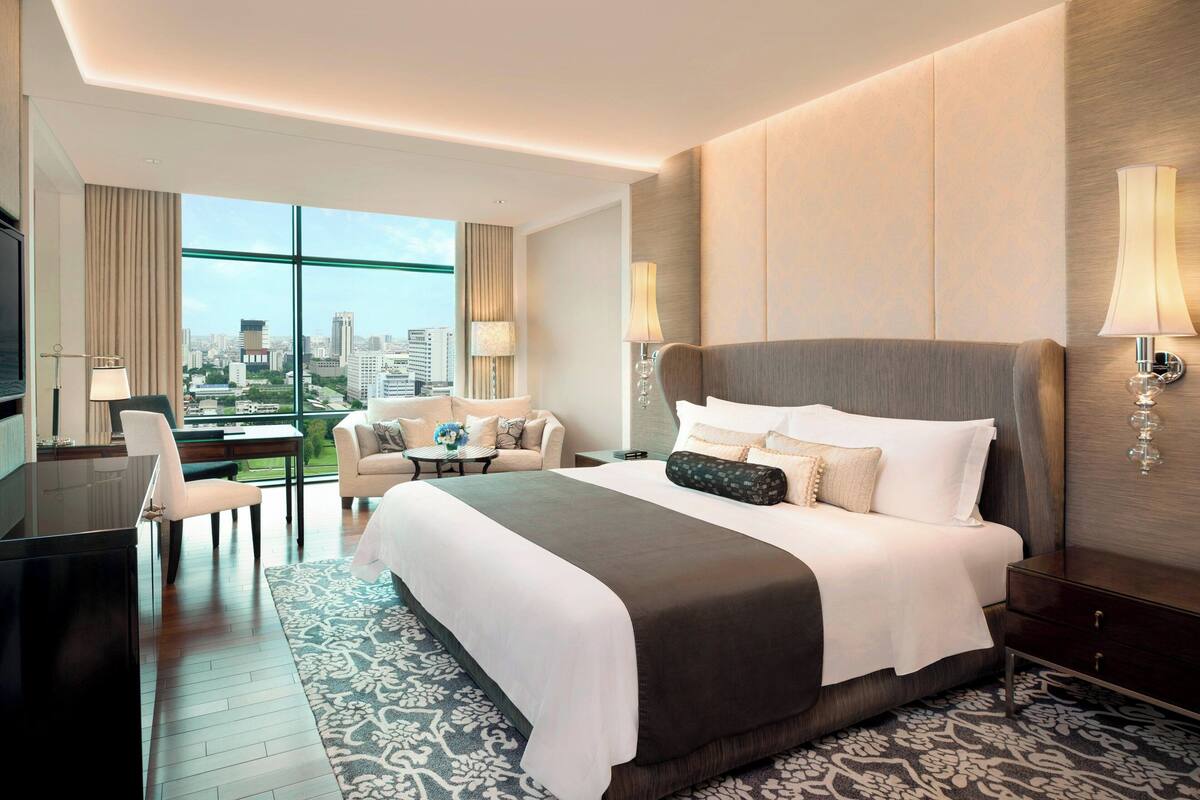 A modern hotel room with a large bed, a desk, a sofa, and a view of the city.