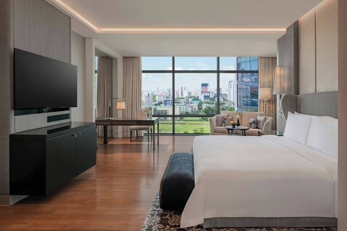 A modern hotel room with a large bed, a flat-screen TV, a desk, and a city view.