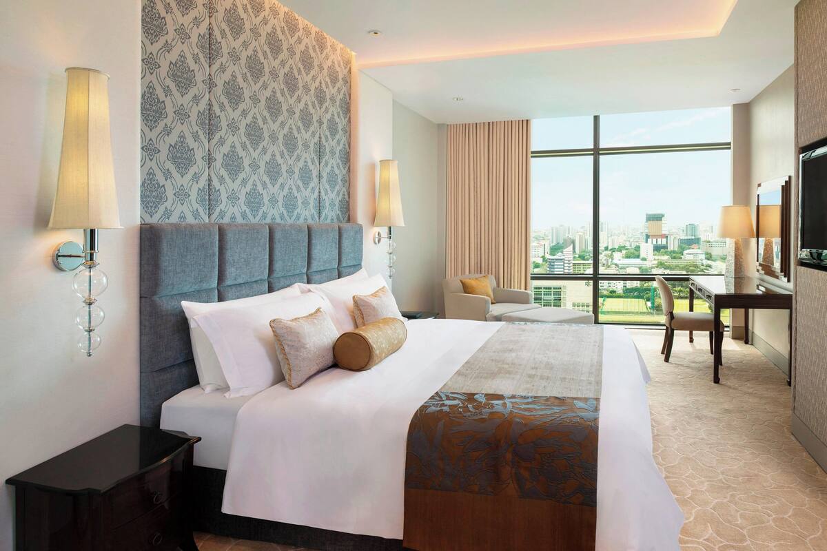 A hotel room with a large bed, two bedside lamps, a desk, and a chair.