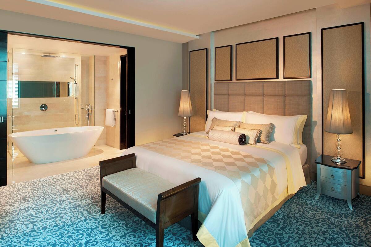 A modern hotel room with a large bed, a separate sitting area, a bathtub, and a large mirror.