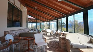 An open-plan lounge with stone flooring, wooden ceiling beams, and large windows offering mountain views. - Lecadin Hotel (Karpenisi)