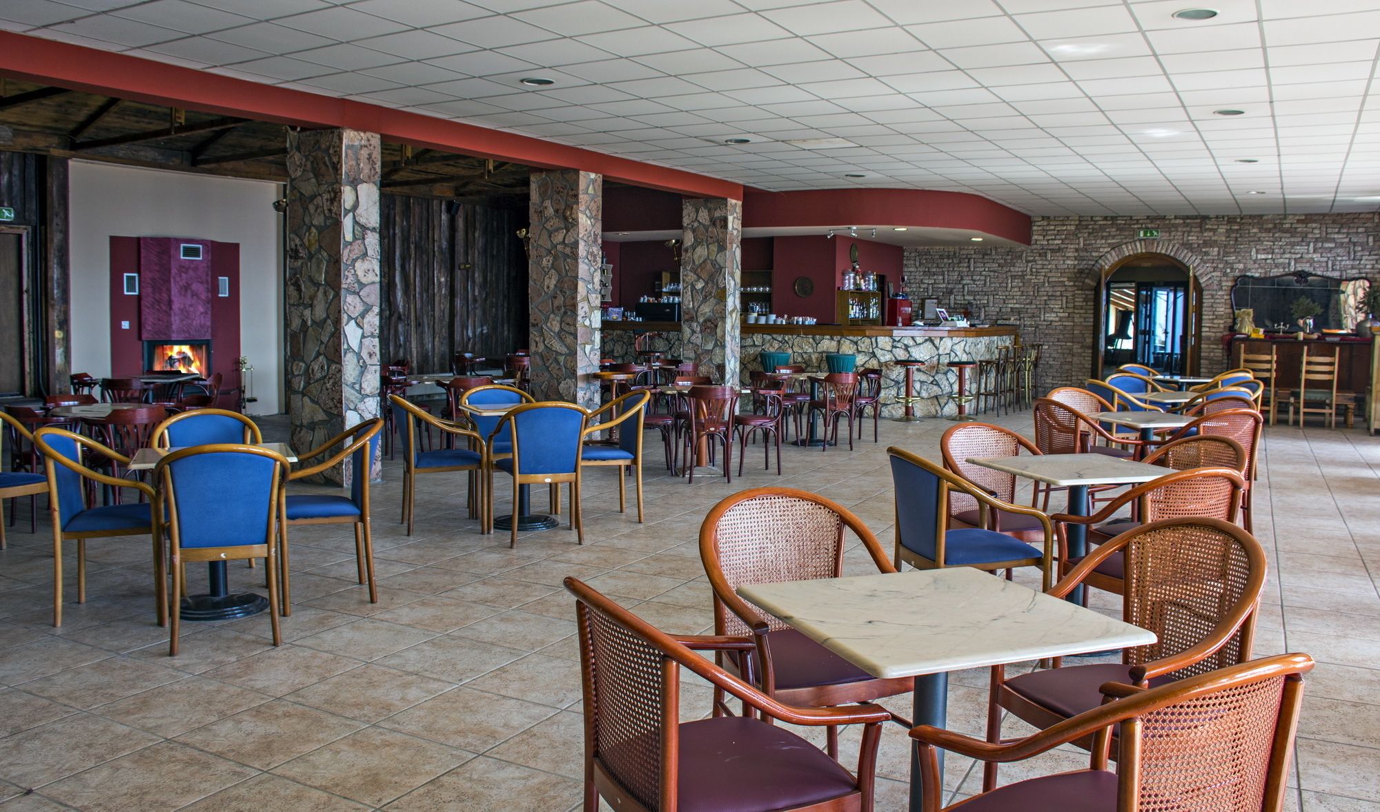 Un vaste espace de restauration intérieur, doté de nombreuses tables et chaises, d’un mur en pierre et d’un bar.
