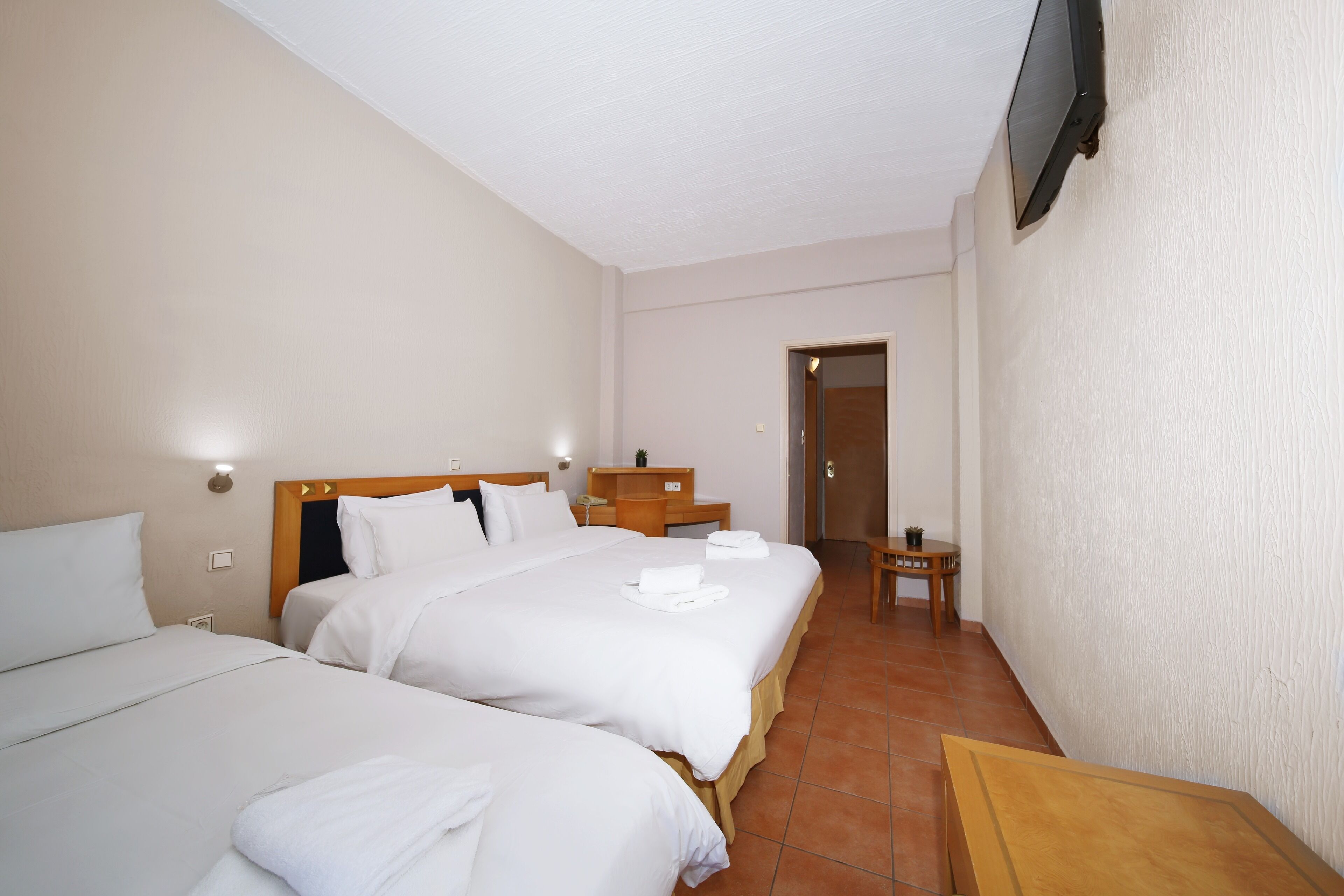 Une chambre d’hôtel avec deux lits, une table de chevet en bois, une petite table et un téléviseur fixé au mur.
