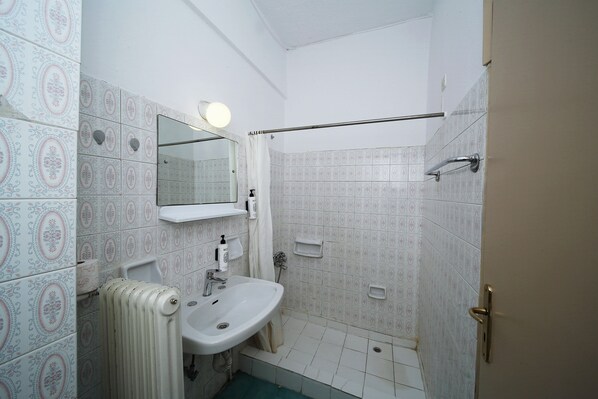 A bathroom with patterned tiles, a sink, a mirror, a towel rack, and a shower area.