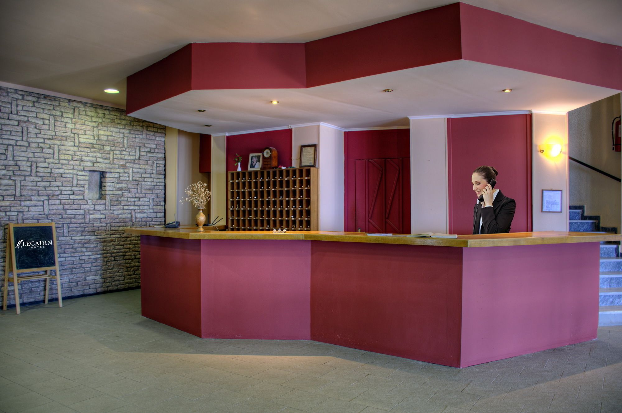 A reception desk with a red and white color scheme, a stone wall, and a sign for LeCadin Hotel.